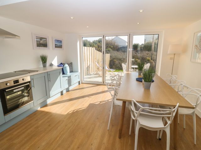 A kitchen and dining area with blue cabinets wooden floor and a wooden table with white chairs at 3 Lon Y Dryw in Trearddur Bay