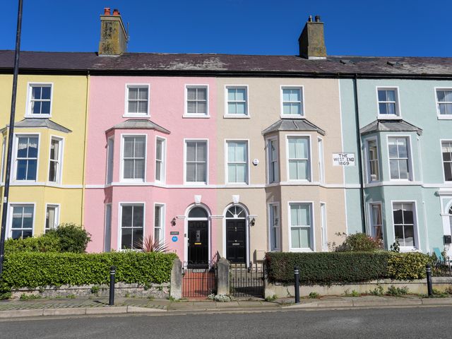 A row of pastel-colored townhouses with hedges and black front doors at Lluest in Beaumaris