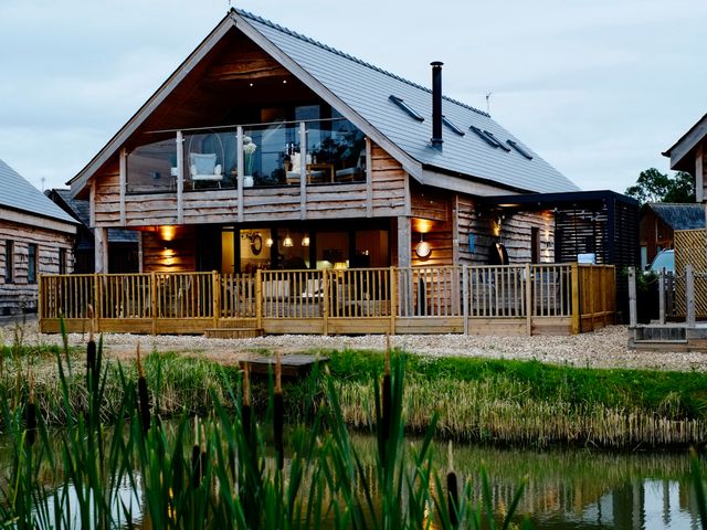 A wooden house with a balcony and outdoor seating near a pond at Lake View Lodge in Thorpe-On-The-Hill