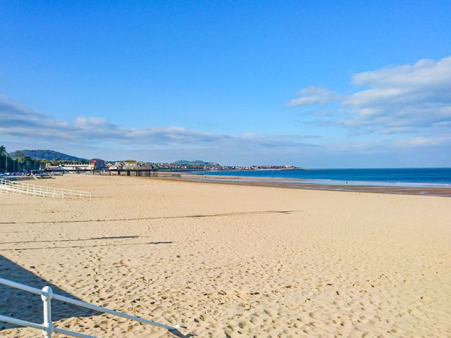A sandy beach with a pier and distant buildings under a blue sky at Ocean View Apartment in Colwyn Bay