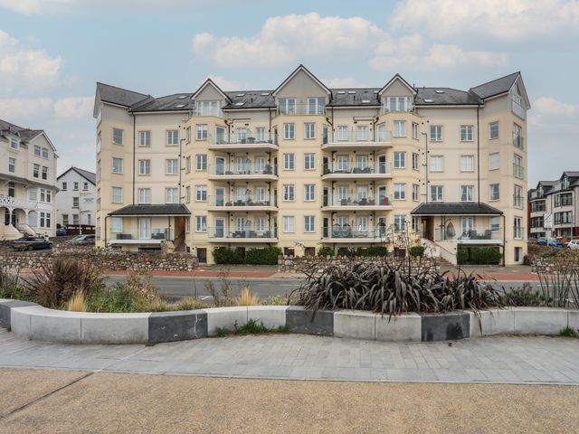 A large apartment building with balconies and multiple windows behind a road and concrete planter at Ocean View Apartment in Colwyn Bay