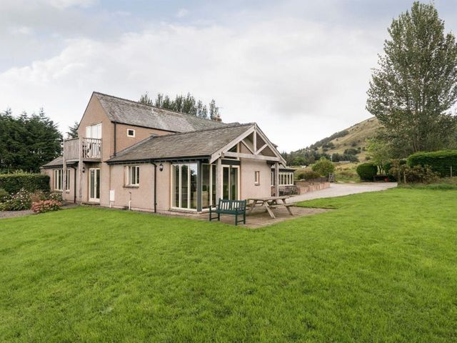 A house with a balcony and patio furniture on a lawn with trees and hills at Beckwood in Troutbeck near Keswick