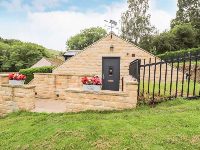 An outdoor area with a stone wall, a dark door, two flower pots with red flowers and a metal railing at Woodlands in Cononley