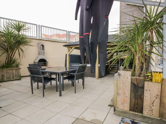An outdoor patio area with a dining table and chairs a built in barbecue two wetsuits hanging and potted plants at Fistral Apres Surf in Newquay