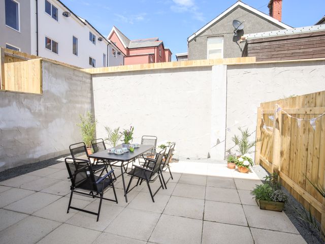 An outdoor patio with a table and six black chairs surrounded by walls and potted plants at Ty Copr Perlog in Criccieth