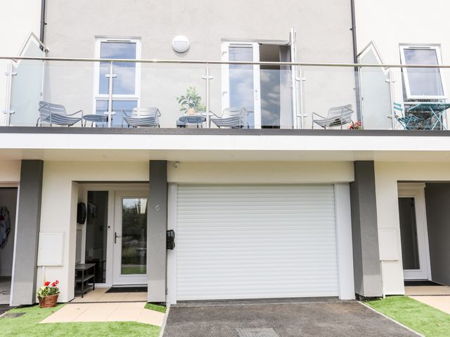 A modern exterior view of a building with a garage door front door balcony and outdoor chairs at Ty Copr Perlog in Criccieth