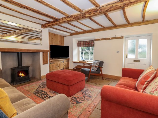 A sitting room with wooden beam ceiling a wood burning stove sofas and a television at 3 Settlebeck Cottages in Sedbergh