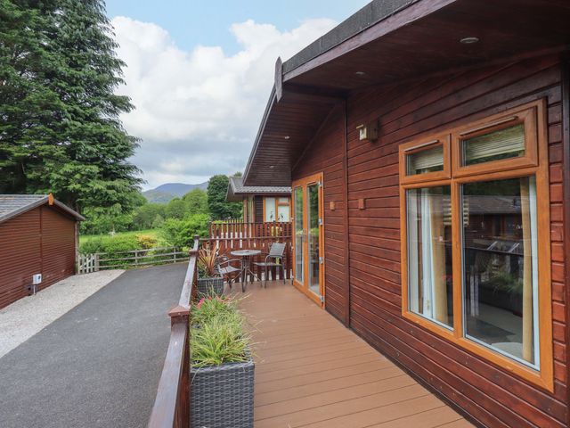 A wooden balcony with a table and chairs overlooking a driveway and green trees at Pheasant's Nest Kirkstone 11 Limefitt Park near Windermere