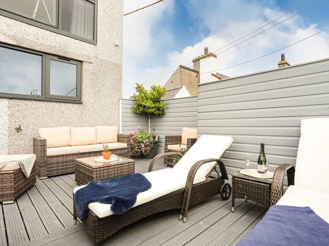 An outdoor patio with wicker furniture including lounge chairs a sofa a coffee table and a side table with a bottle and glasses at Arlan in Benllech