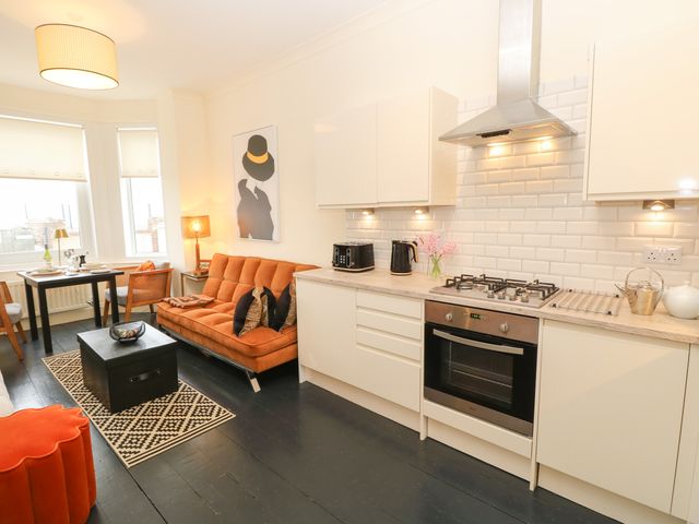 A kitchen and living area with white cabinets and an orange sofa at No 5 Cliffview in Ventnor