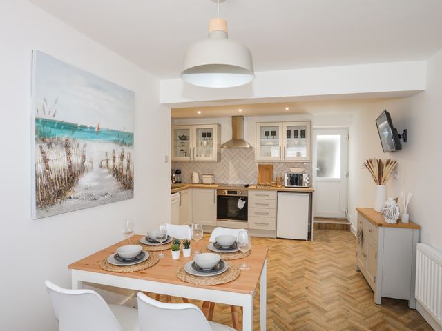 A kitchen and dining area with a wooden table set for four and a painting on the wall at A Mor in Newborough