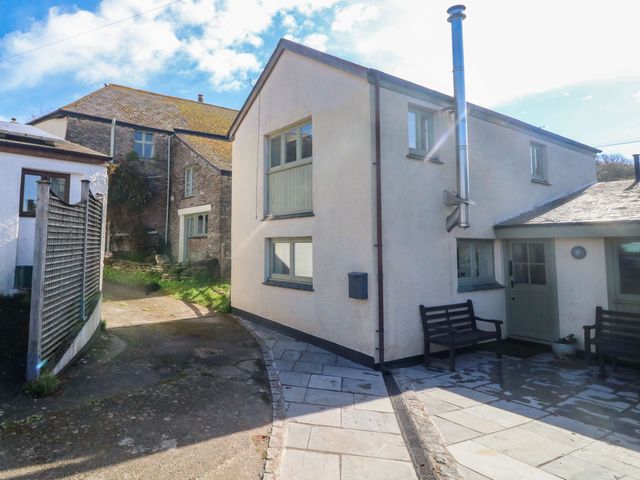 Exterior view of two connected houses with benches outside on a paved area at Wrens Nest in Slapton
