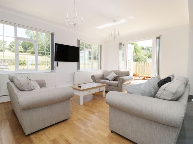 A living room with three grey sofas a wooden coffee table two chandeliers and a wall-mounted TV at Castle Top Retreat in Nettleton Lincolnshire