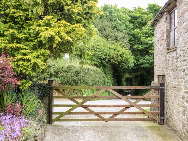 A wooden gate on a driveway next to a stone building with trees and bushes in the background at Keepers Cottage in Liskeard