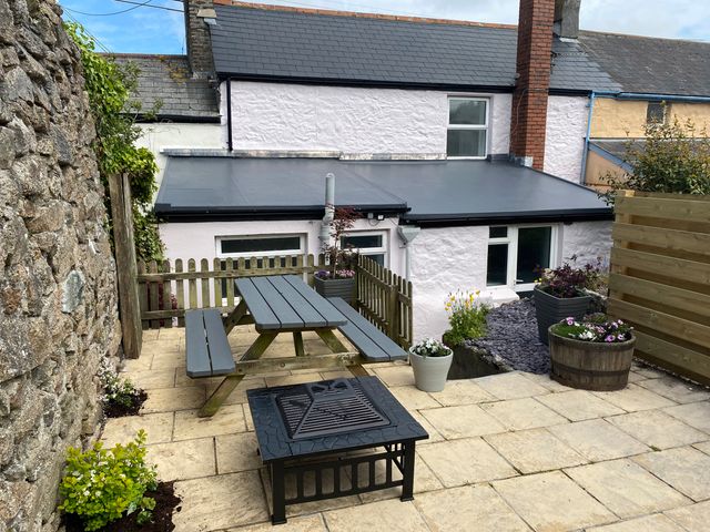 A patio with a picnic table fire pit and potted plants outside a stone house at Miner's Rest in St Day