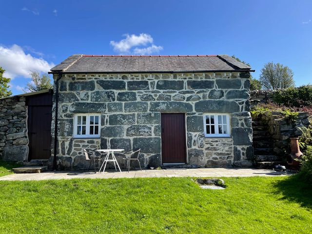 A stone cottage with two windows a door and a small table with two chairs on a patio at Gelli Bach at Gelli Las in Llanbedr