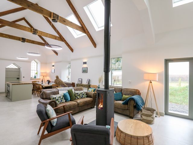 An open plan living and dining area with exposed wooden beams wood burning stove and dining table at Ysgoldy Brynwyre in Llanrhystud