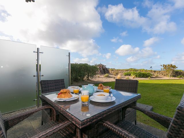 An outdoor patio table with four wicker chairs set with breakfast bowls croissants orange juice and a teapot at Beach Haven in Carbis Bay