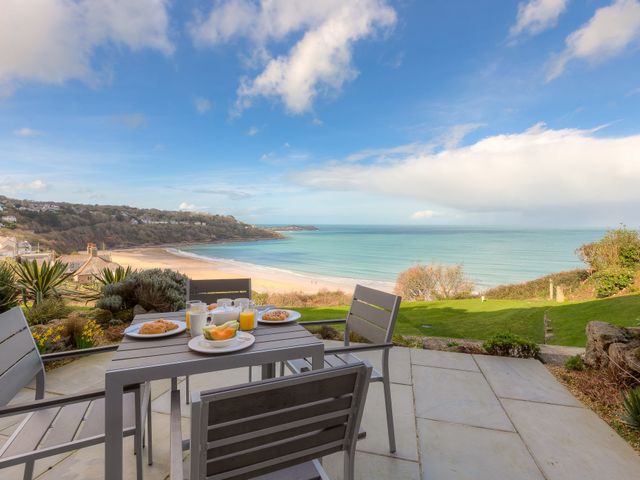 An outdoor patio with a table and chairs set for breakfast overlooking a beach and ocean at Carbis Bay View in Carbis Bay