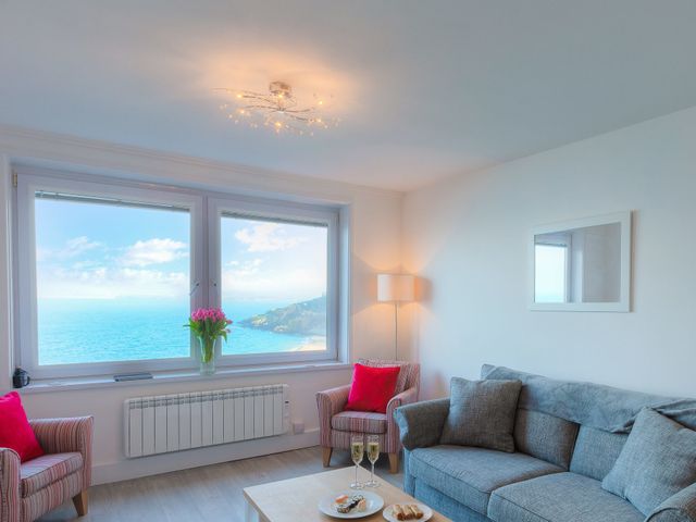 A living room with two armchairs and a sofa near a large window with ocean view at Ocean Shore in St Ives