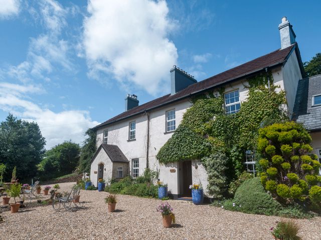 An exterior view of a two story building with ivy on the walls and potted plants on a gravel courtyard at Brokan @ Fourwinds in Meldon near Okehampton