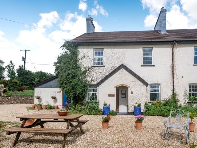 The exterior of a two-story house with a gravel yard a wooden picnic table potted plants and a metal chair at Tor View @ Fourwinds in Meldon near Okehampton
