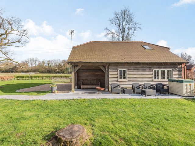 A wooden building with a covered porch bench patio furniture and green grass in a rural setting at Red Kite Cottage in Froxfield Hampshire