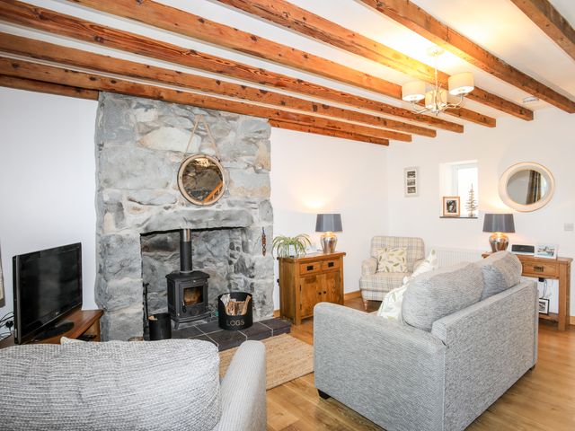 A living room with exposed wooden beams stone fireplace wood burner gray sofas and armchair at Gyda'r Llif in Llanystumdwy near Criccieth