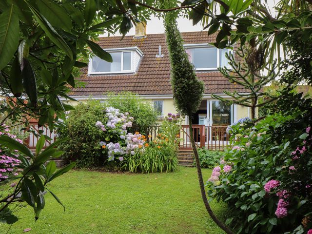A garden with flowering bushes and a lawn in front of a house with a tiled roof and patio in Pencoys Mullion