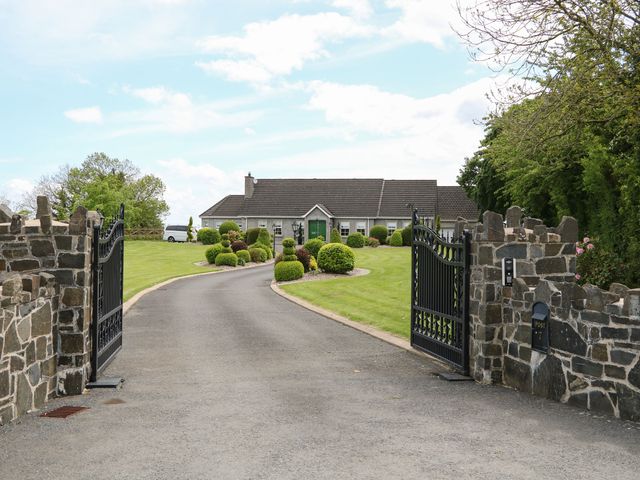 A driveway with open black gates leading to a house with trimmed bushes and green lawn at The Hideaway in The Loup near Moneymore