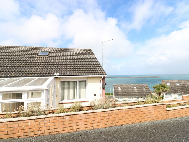 A semi detached house with a sloped tiled roof and a brick wall in front overlooking the sea at Murmur y Mor in Fishguard