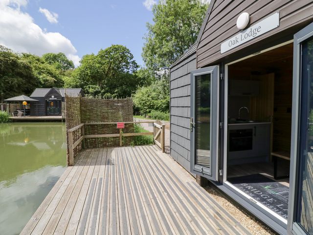 An outdoor view of a lodge by the water at Oak Lodge At Bridge Lake Farm & Fishery Chacombe