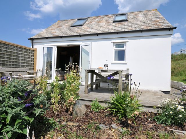 An outdoor view of a cabin with a table and flowers at Cartway Cabin Port Isaac