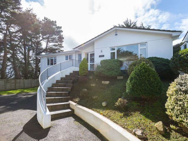 A white house with a curved staircase and shrubs in the front garden at Beaches in Polzeath