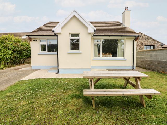 A backyard with a wooden picnic table and a cream colored house with multiple windows at Chalfonts Cottage in Trefin near Penparc