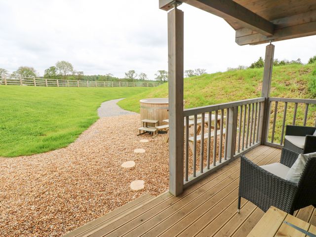 A wooden deck with two chairs and a railing overlooking a gravel pathway leading to a wooden hot tub and grassy area at Foxes Den in Winston near Staindrop