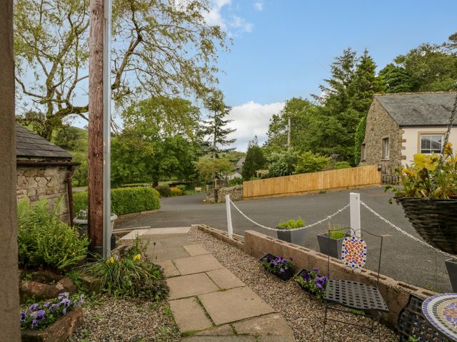 An outdoor patio area with a stone path flower pots and a chair next to a paved road and stone buildings at Swaledale Watch Garden Annexe in Caldbeck