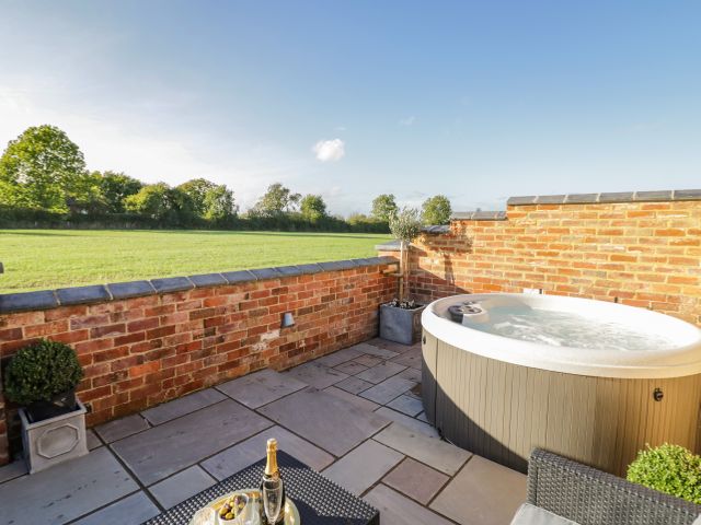 A patio with a hot tub and a table with champagne glasses and snacks at The Hyde in Armscote near Newbold on Stour