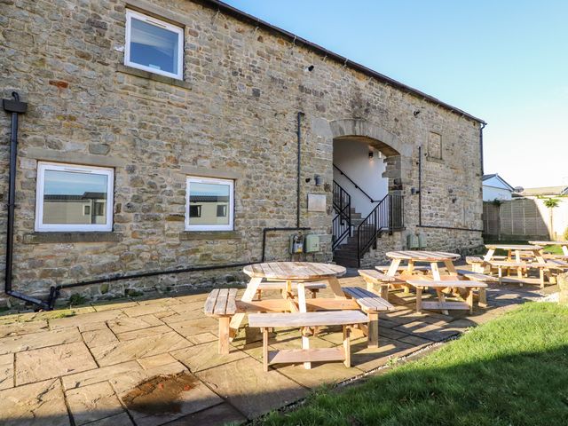 An outdoor patio area with wooden picnic tables in front of a stone building with windows and an arched entrance at Malham in Long Preston