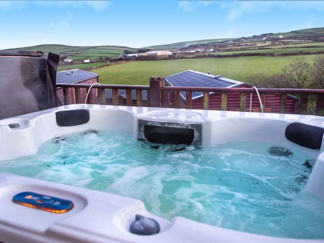 An outdoor hot tub with water jets and headrests overlooking green fields and rooftops at Chi Prenn Byhan in Tintagel