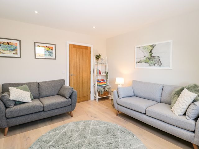 A living room with two sofas a round rug a wooden door and a shelf with books and a lamp at Kimberlin in Chiswell On Portland