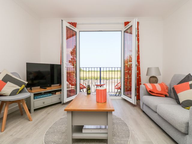 A living room with a couch a chair a coffee table and open doors leading to a balcony at Azure in Carbis Bay
