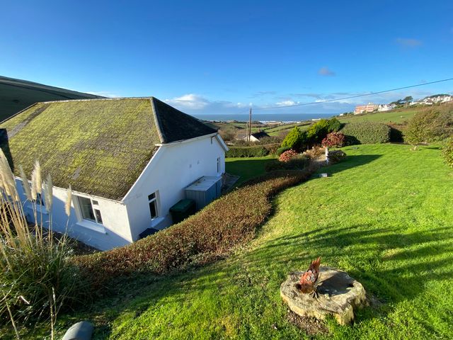 An outdoor garden with a white house a hedge green lawn and a distant view of the sea at Surf View in Woolacombe