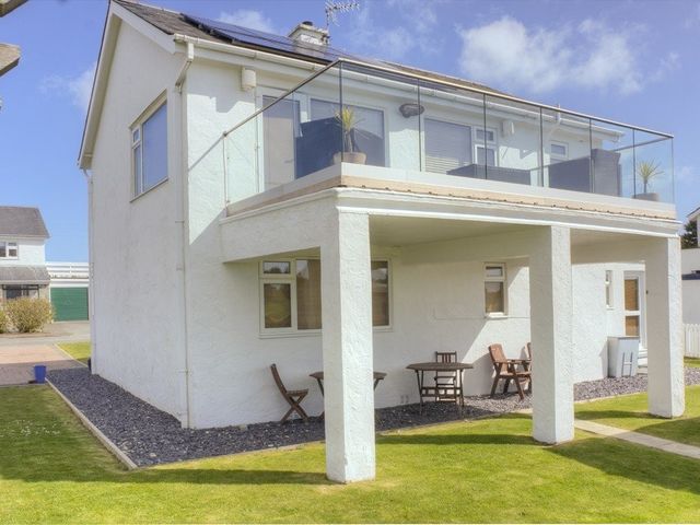 A two story house with a balcony and outdoor chairs and tables at Eleri in Abersoch