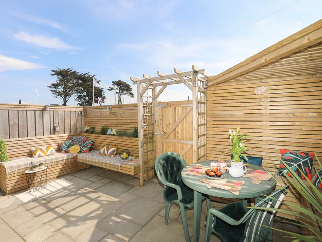 A fenced outdoor patio with built in wooden seating and a round table with chairs at Lle Te in Abersoch