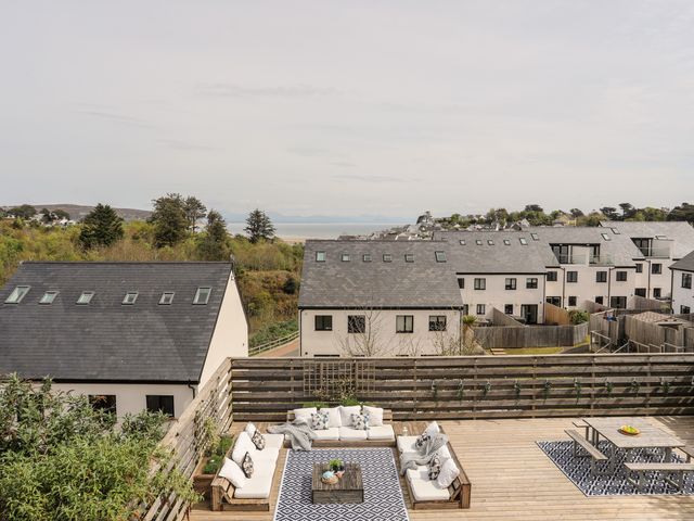 A rooftop deck with outdoor seating and a dining table overlooking residential rooftops and greenery at Nyth Y Fran in Abersoch
