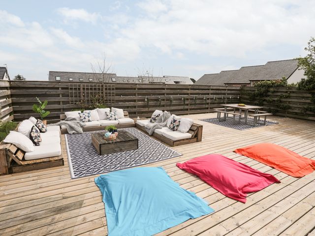 An outdoor wooden deck with cushioned seating area a wooden table and multicolored bean bags at Nyth Y Fran in Abersoch