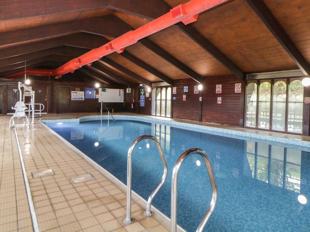 An indoor swimming pool with metal handrails and wooden ceiling beams at Harcombe House Bungalow 9 in Chudleigh