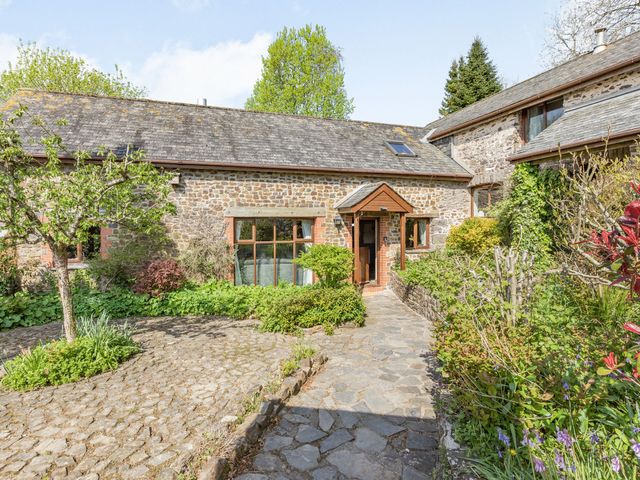 A stone house with a tiled roof and garden path surrounded by greenery at Hazel Barn in North Molton