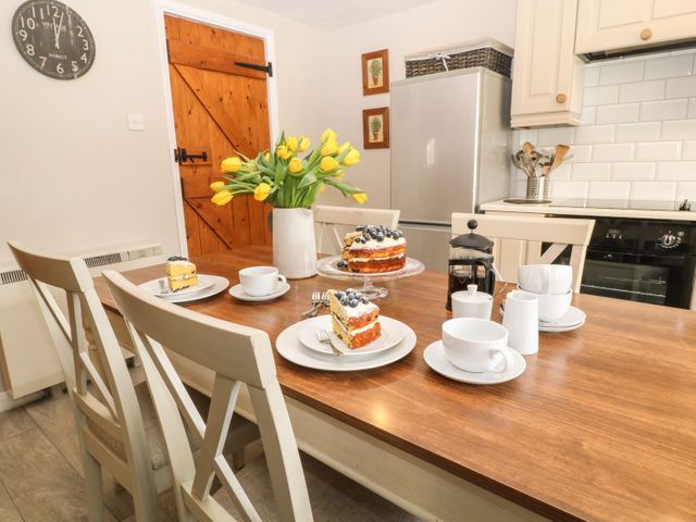 A kitchen with a wooden table set with cake slices coffee cups a vase of yellow flowers and a French press at Beechcroft Cottage in North Molton